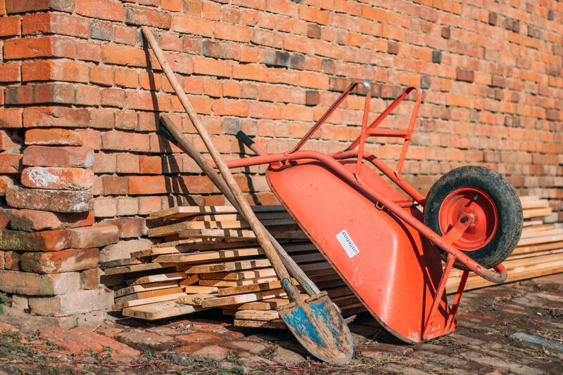 Wheelbarrow, shovel and stacked timber beside a red brick wall on a work site — brickwork in Canterbury