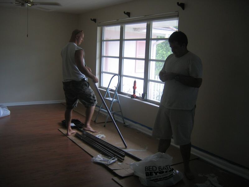 Two workers fitting curtain rods by a large window with a stepladder and drill — curtain rail installation Rolleston