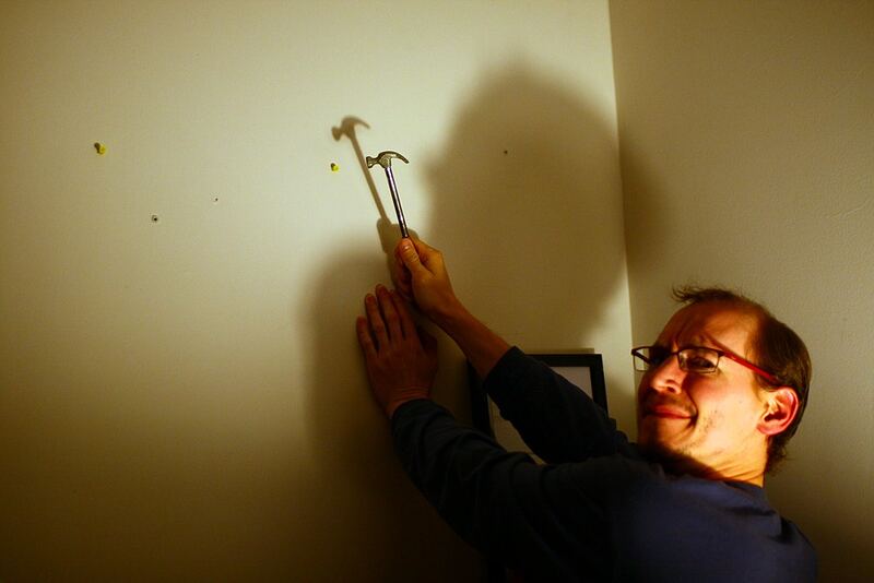 Homeowner hammering a nail into a living-room wall to hang a picture — picture hanging in Selwyn