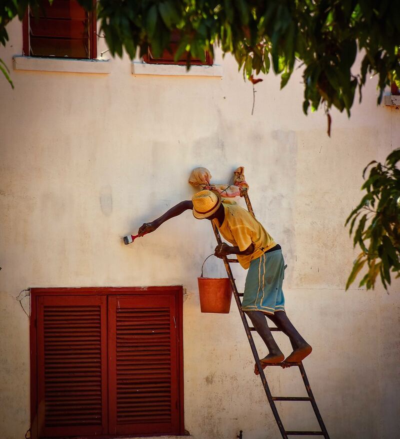 House painter on a ladder brushing paint onto an exterior wall — plastering and painting in Rolleston