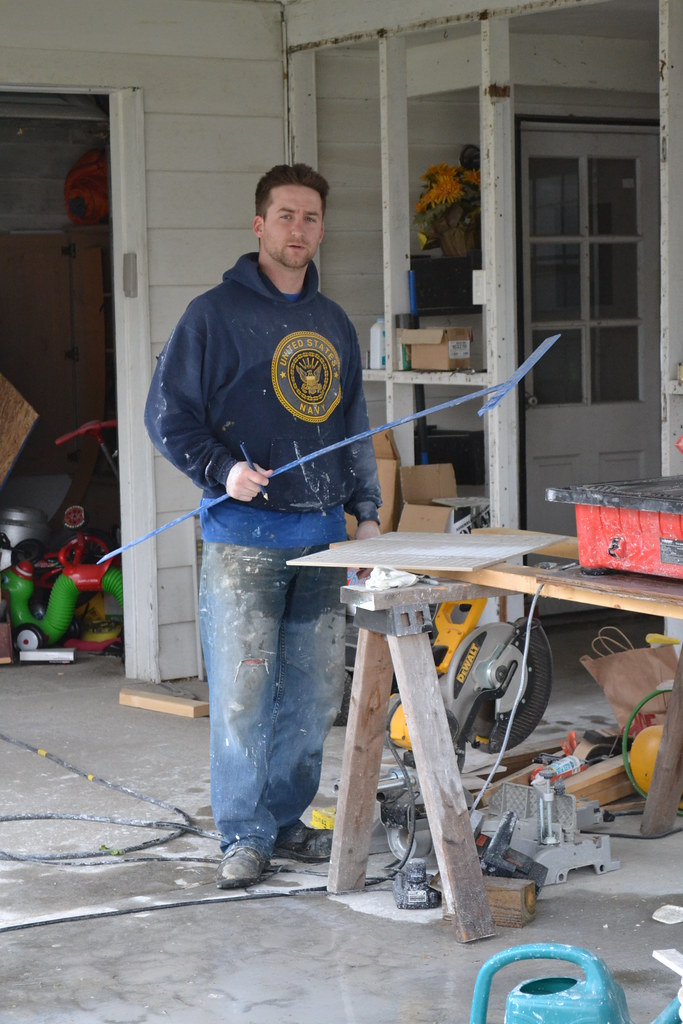 Handyman in paint-marked work clothes with power tools in a home workshop — property maintenance Rolleston Selwyn