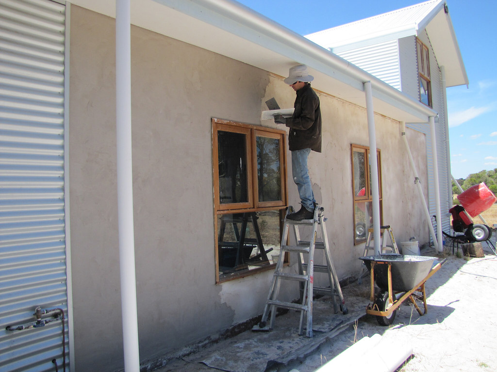 Tradesperson on a ladder applying plaster render to a house exterior wall — plastering work in Canterbury